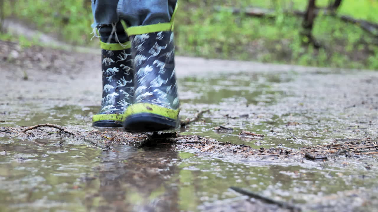 niño caminando por un charco fangoso con botas