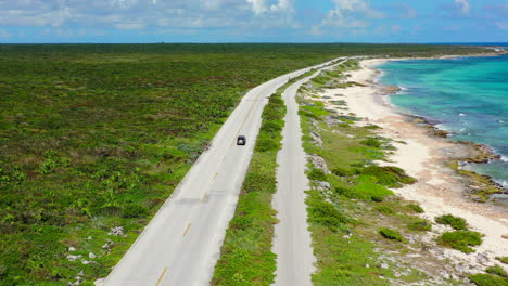 Panorámica-Aérea-De-Una-Isla-Verde-Y-Exuberante-Con-Conducción-De-Automóviles-En-Una-Larga-Carretera-Junto-Al-Mar-En-Cozumel,-México