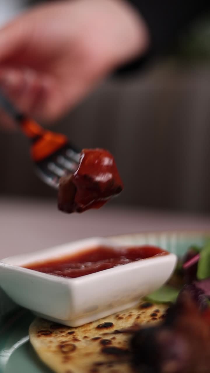 Person eating a piece of grilled meat with sauce
