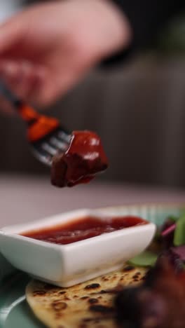 persona comiendo un pedazo de carne a la parrilla con salsa