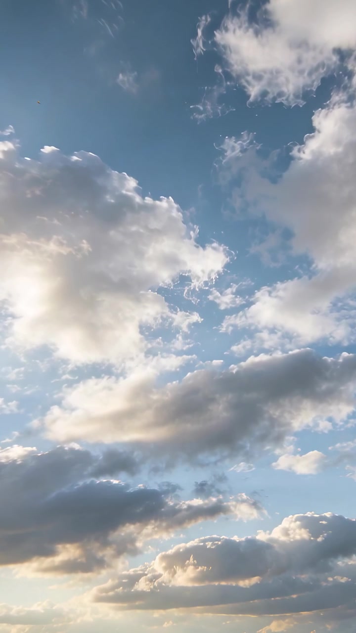 Video verticale: Nuvole cumuliformi che fluttuano e si illuminano al sole su un cielo blu, con il sole basso.