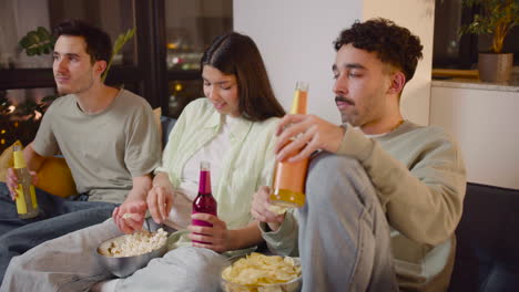 Drei-Freunde-Sehen-Sich-Interessante-Filme-Im-Fernsehen-An,-Sitzen-Auf-Der-Couch,-Essen-Popcorn-Und-Chips-Und-Trinken-Limonade-2