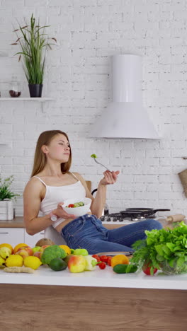 young woman is relaxing in the kitchen. beautiful girl sitting in the nice kitchen and eating fresh food. fresh organic fruit and vegetables. healthy food concept. vertical video