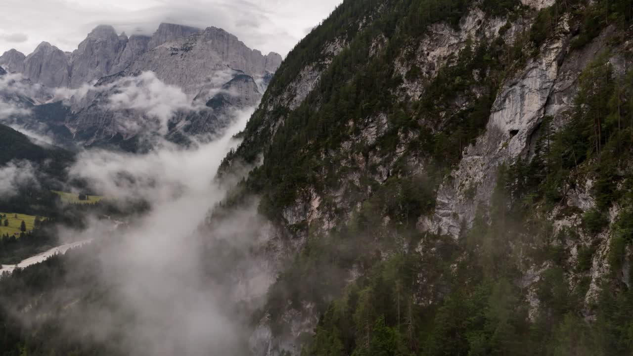 Drone flies through clouds over green Alps mountains on a cloudy day showcasing natural beauty