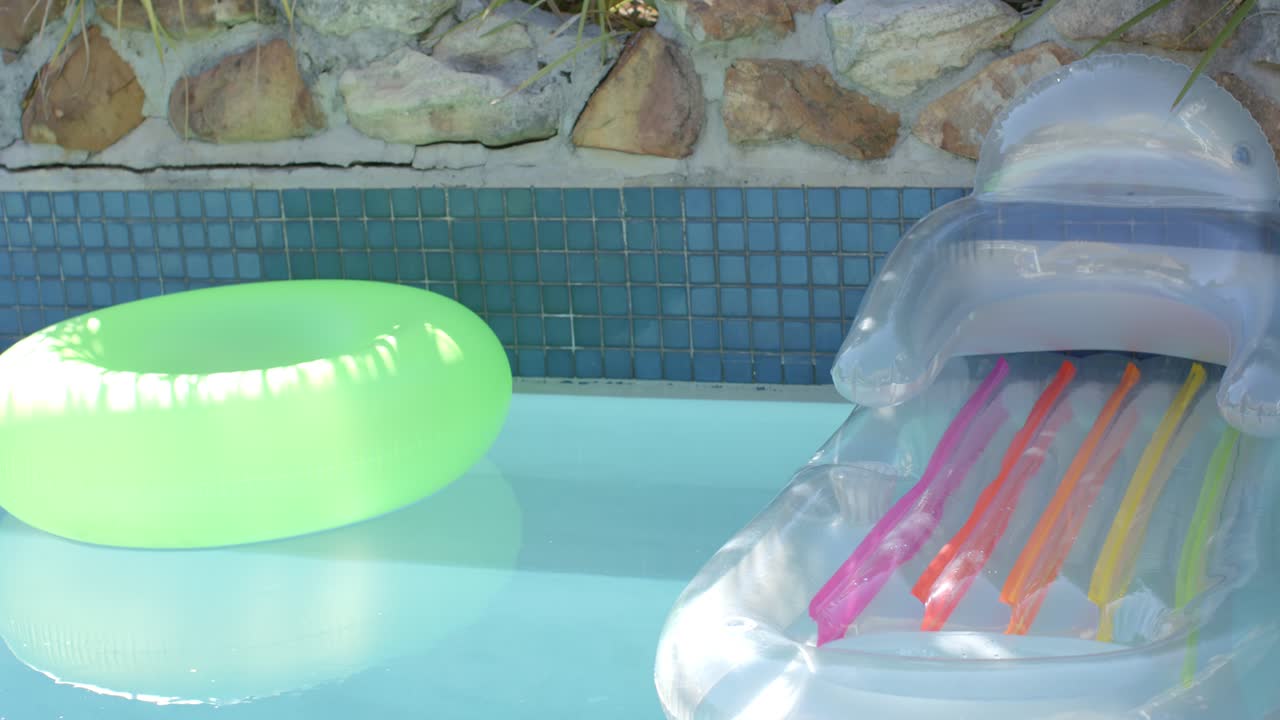 Pool current is nudging neon swim ring left while clear lounge is drifting, showing colorful strips