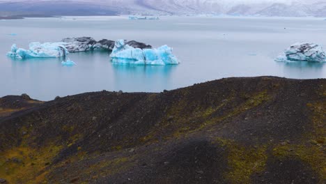 Drohnen-Luftaufnahme-Der-Herrlichen-Jokulsarlon-Lagune-In-Island-Mit-Ihren-Auf-Der-Wasseroberfläche-Schwimmenden-Eisbergen-Und-Ihrem-Beeindruckenden-Gletscher-Am-Boden,-Bewölktes-Wetter