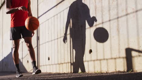 hombre afroamericano en forma haciendo ejercicio al aire libre en la ciudad, caminando rebotando baloncesto