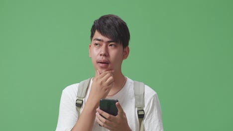 휴대폰을 사용하고 생각하고 녹색 스크린 스튜디오에 지표손가락을 올리는 아시아 남성 학생의 클로즈업