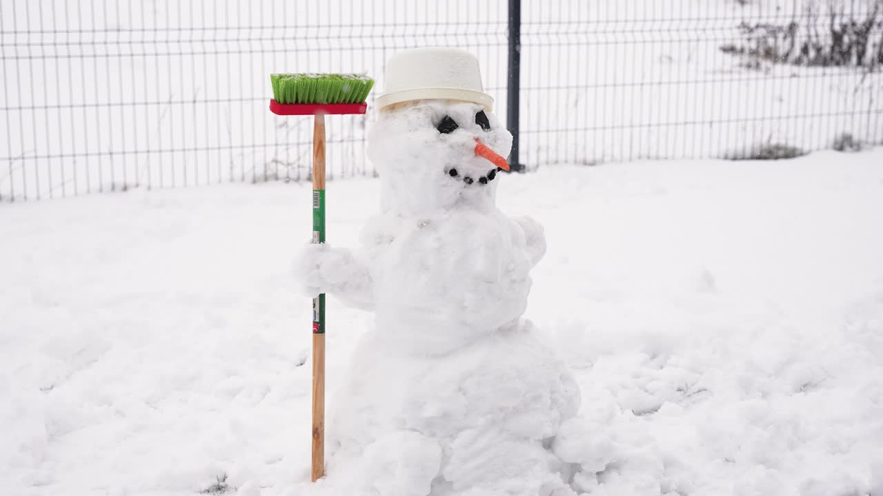 En dejlig snemand med en gulerodsnæse og spand som hat, der holder en kost på en sneklædt mark. Denne finurlige scene er fanget på en kold, overskyet dag og fremkalder vintermagi og barndomsglæde
