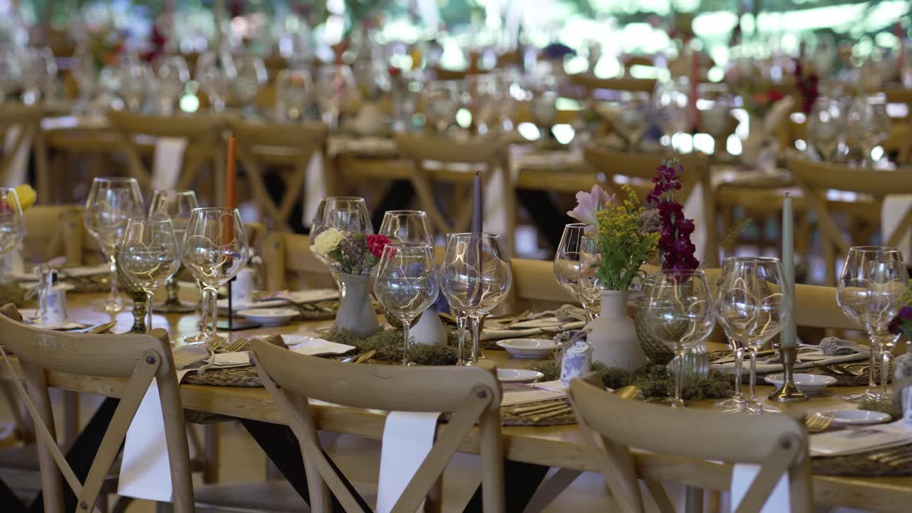 Long wooden tables set with glassware, floral centerpieces, and elegant decor