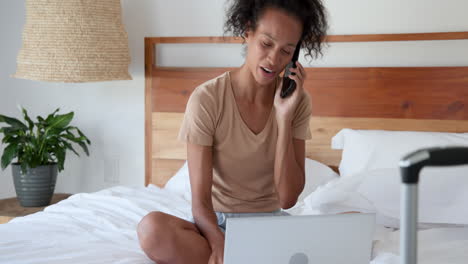 woman sitting on bed using smartphone and laptop, multitasking at home