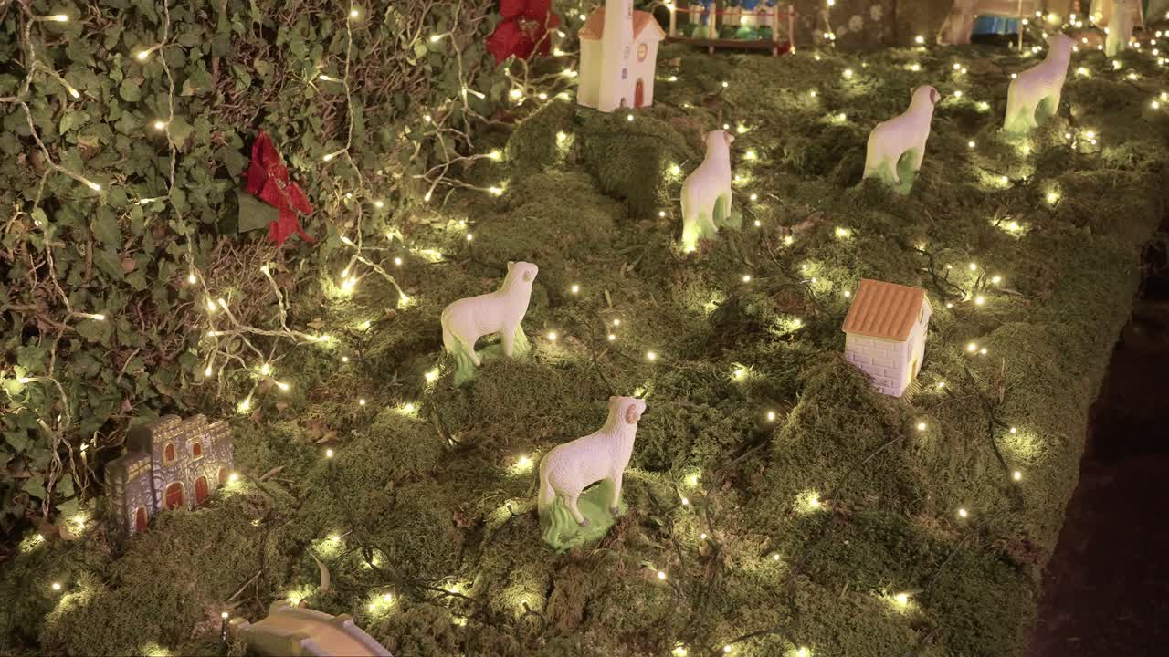 festive nativity village with glowing fairy lights, miniature houses, and sheep figurines on moss