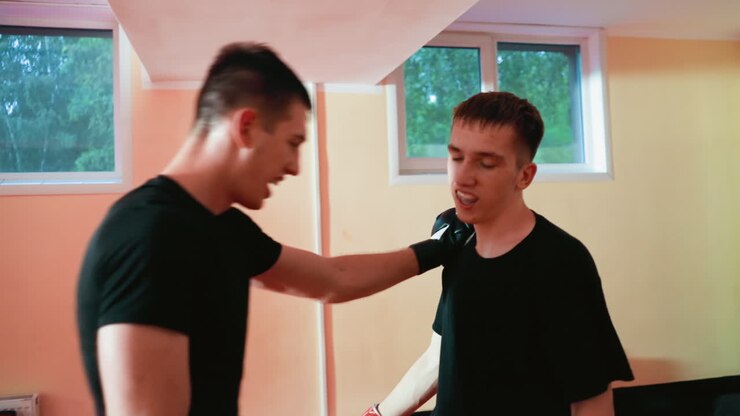 Boxers engaged in sparring session on red mat inside gym, wearing gloves, facing each other throwing punches with focus and determination, practicing combat stance, preparing for strike with intensity