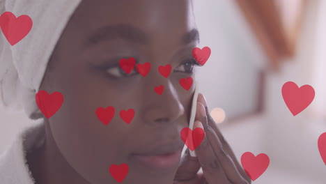 animación de corazones rojos sobre feliz mujer afroamericana limpiando la cara en casa