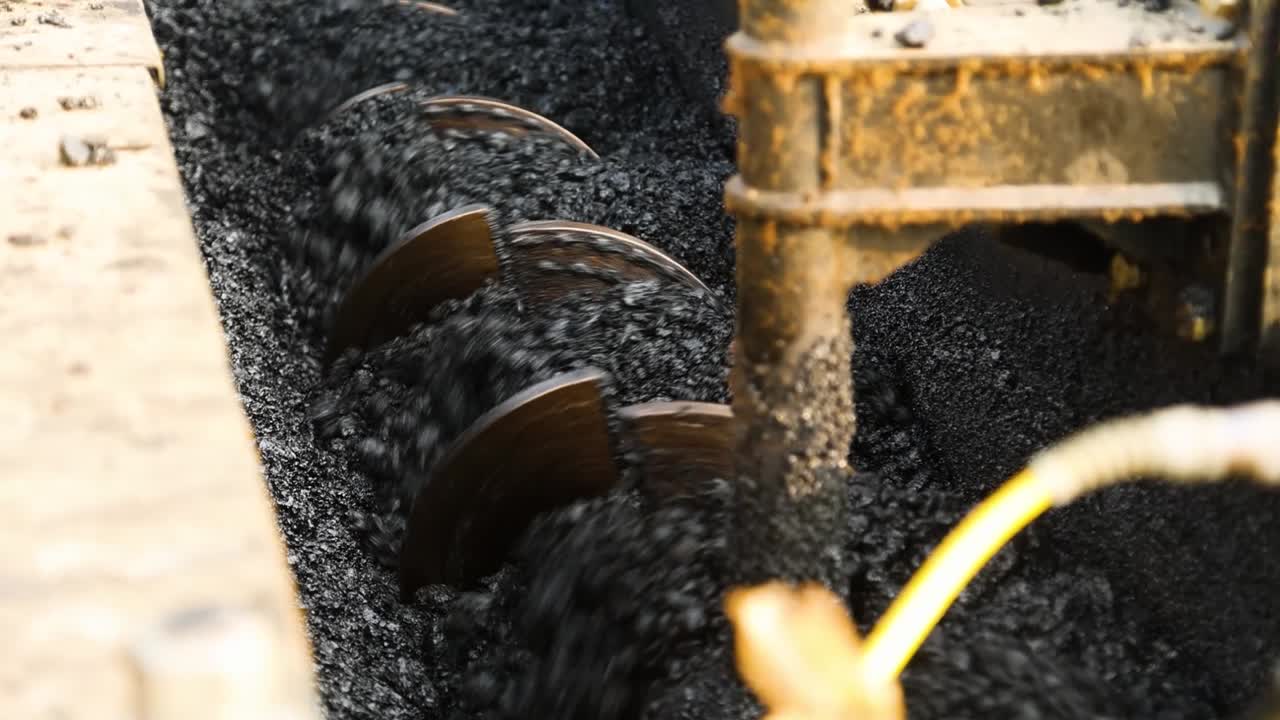 Close-up of an asphalt paver machine in China. The auger turns and spreads hot asphalt during a road construction project