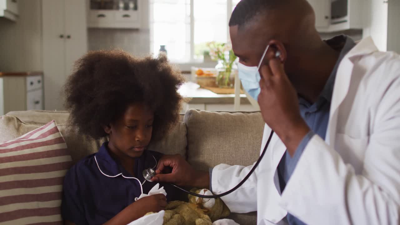 médecin afro-américain portant un masque facial utilisant un stéthoscope pour traiter une fille malade à la maison