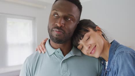 Portrait-of-happy-diverse-couple-wearing-jacket-and-shirt-and-embracing-in-living-room