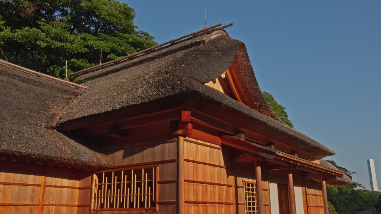 The beautiful thatched roof and wooden facade of a historic Japanese building, bathed in warm sunlight. Serene traditional view.