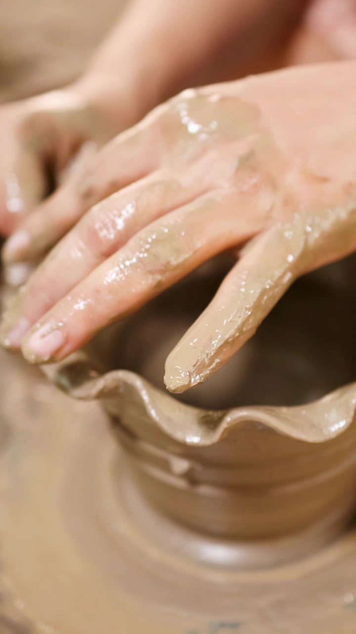 Primo piano delle mani di un artigiano che modellano argilla umida in una ciotola decorativa su un tornio