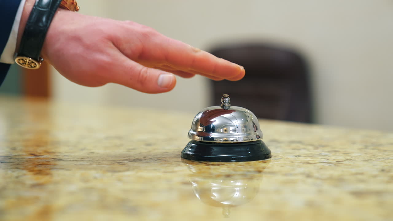 Calling the receptionist. Hand of a tourist in the reception of a hotel presses the bell button. Close-up.