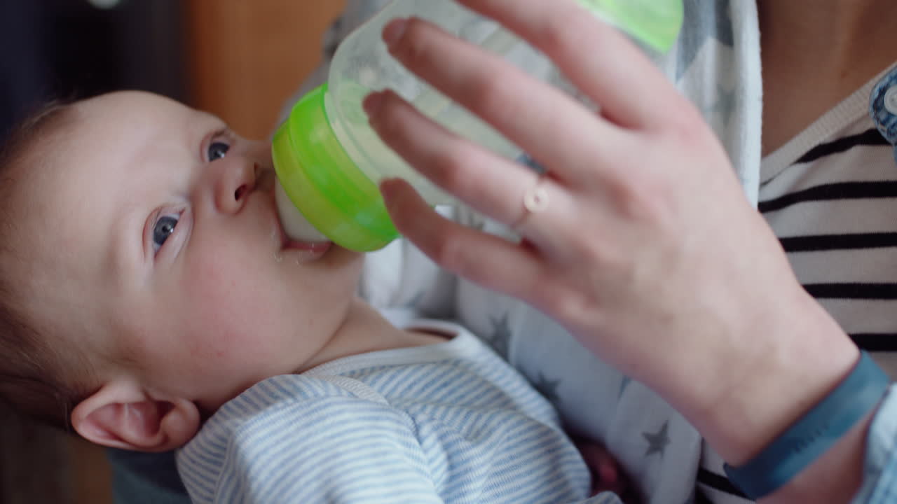 madre joven alimentando bebé infeliz bebiendo de la botella de leche llorando bebé inquieto en casa con madre cansada