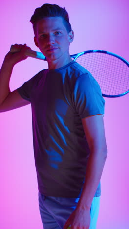 vertical video studio portrait of male tennis player with racket and ball against low key colourful mixed lighting