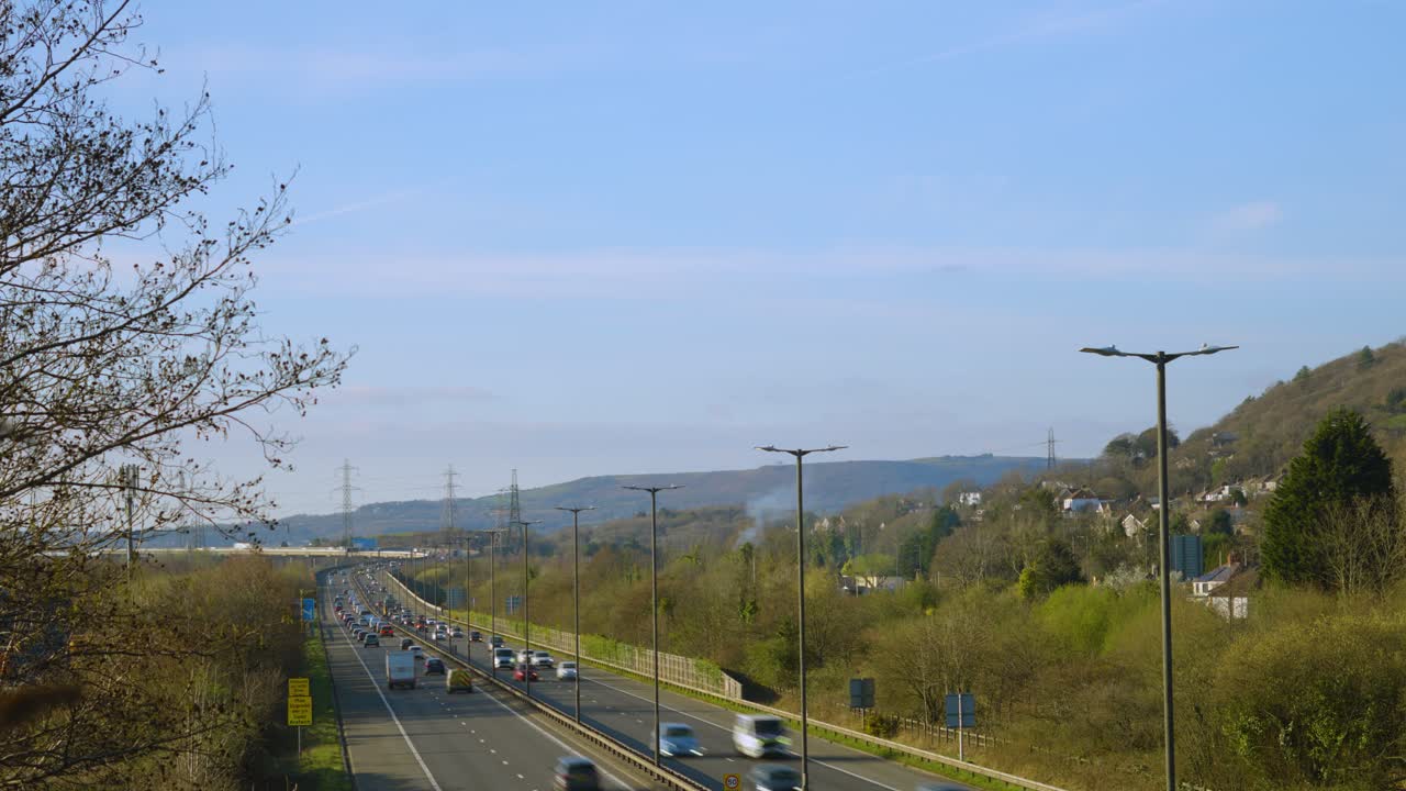 Fast Timelapse of Cars and Trucks Travelling Along M4 Motorway Road in Wales with Motion Blur with Fire Burning Smoke and Trees in Background. Traffic Congestion Commuting Footage.