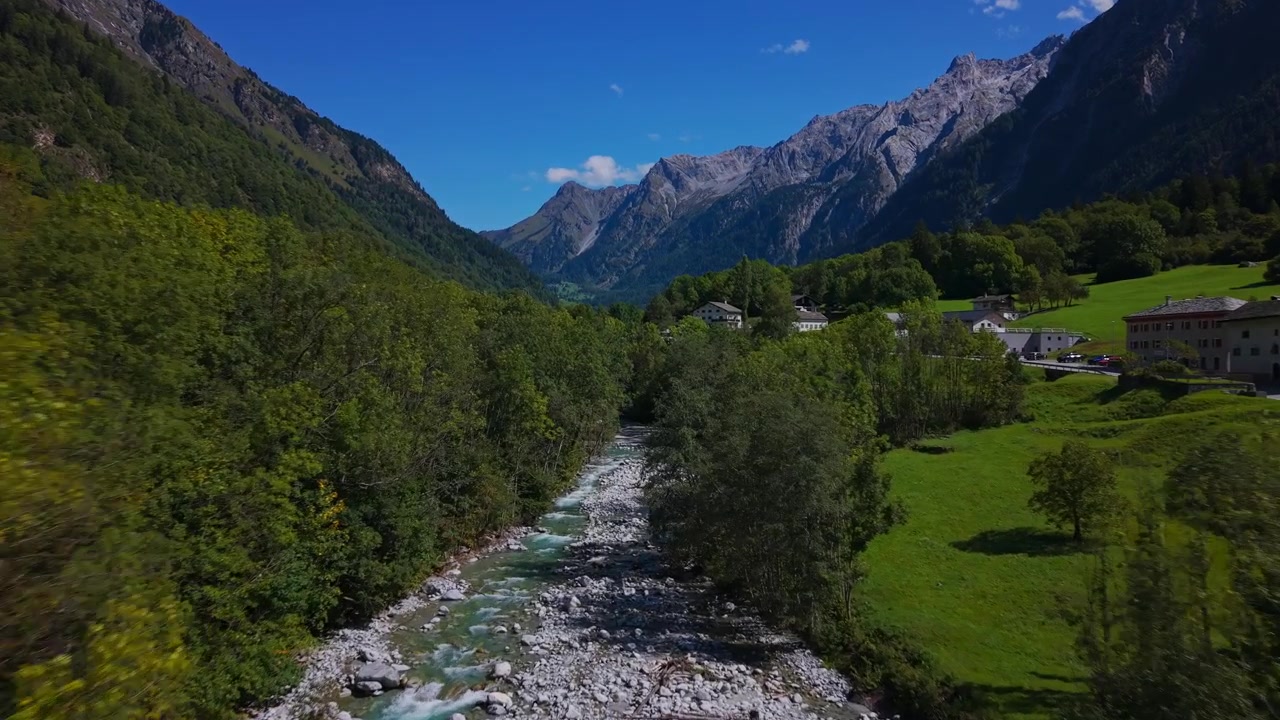 Vista drone che sorvola un fiume incontaminato e una lussureggiante foresta verde con le Alpi svizzere sullo sfondo nella Valle di Bregaglia, Svizzera. Avanzamento aereo