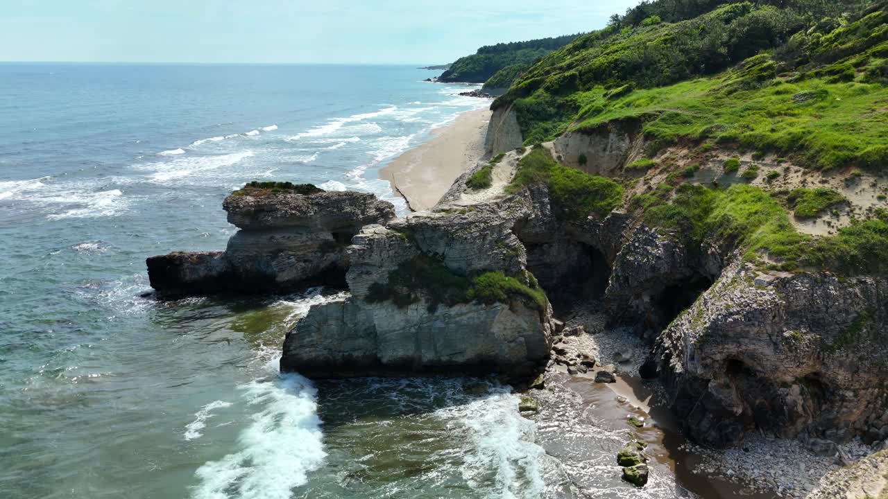 Aerial view of rocky coastline with waves crashing on a sunny day