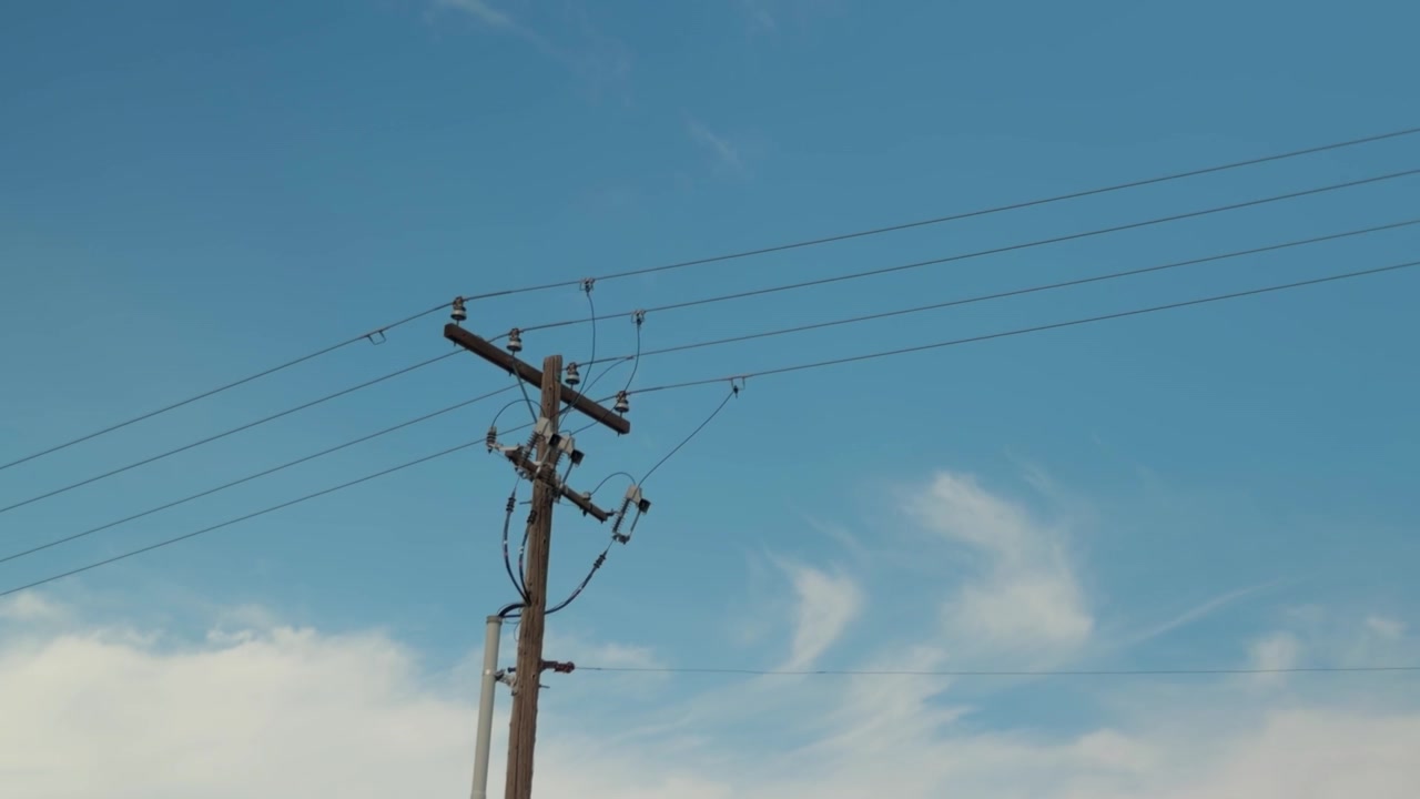 Slow pan across a wooden utility pole and overhead power lines.