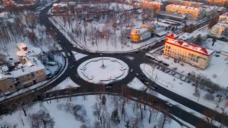 4k aerial view of roundabout road with circular cars in snow covered small european city at winter sunset