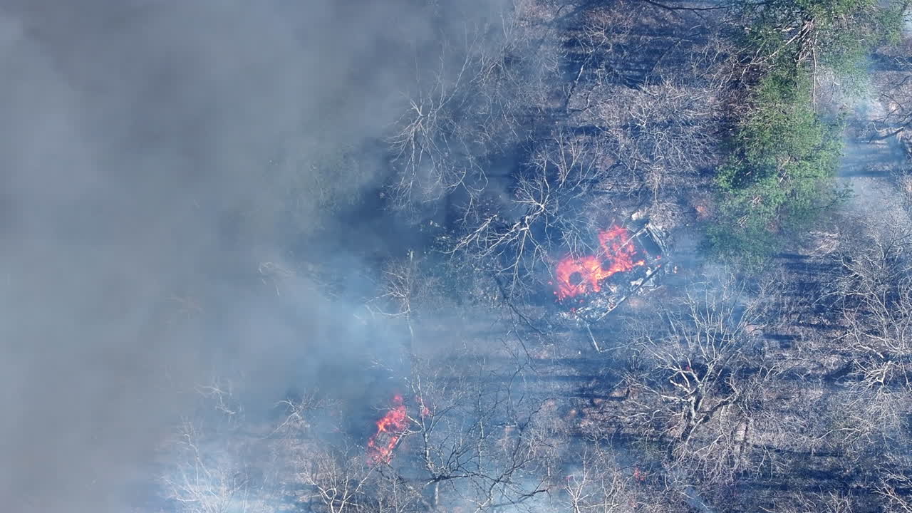 Top down aerial footage that is rotating around a camper that is on fire in the forest.