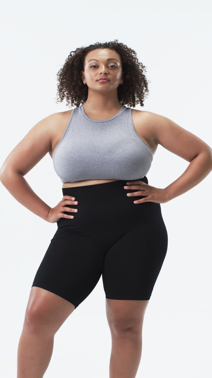 Vertical video: Confident plus size woman in activewear posing with hands on hips