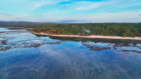 Drone-shot-panning-along-the-shoreline-of-Grajagan-bay,-on-the-island-of-Java-in-Indonesia,-showing-extensive-coral-reef-and-crystal-clear-water