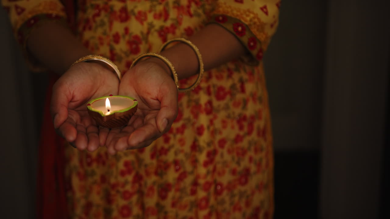 Holding lit diya, Indian woman in traditional dress celebrating festival at night