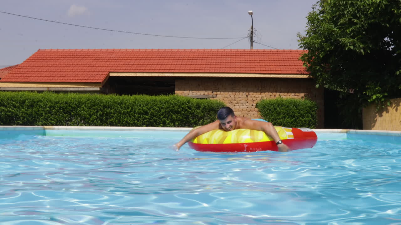 persona flotando en una piscina al aire libre en un brillante día soleado con una casa en el fondo