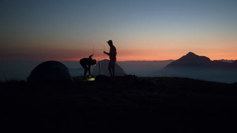 two young friends are preparing their tent in order to sleep on the top of a mountain in the italian alps