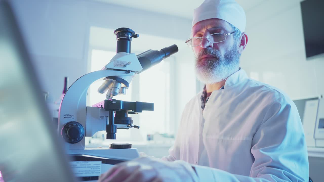 Male Scientist Working with Microscope and Laptop in Modern Laboratory