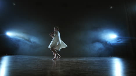 la cámara de zoom se mueve alrededor del escenario con software y humo. chica bailarina bailando en un vestido blanco girando plástico mientras realiza piruetas y rotaciones experimentando emociones y atmósfera dramática.