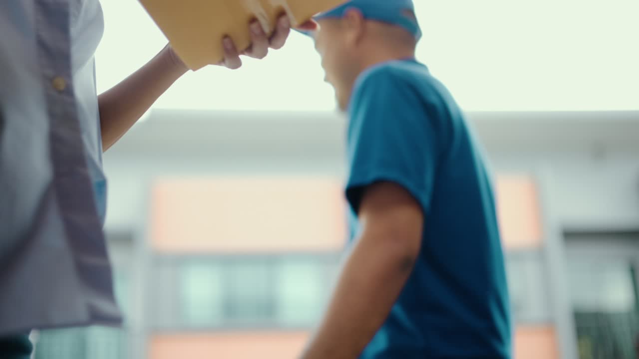 cerrar paquete en la mano de hombre de entrega uniforme azul al cliente frente a la casa con buen servicio de compras en línea. mensajero hombre entregando un paquete postal de caja de cartón a destino.