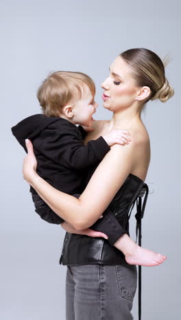 young caucasian woman is holding a little baby boy. mother and son portrait in studio. vertical video.