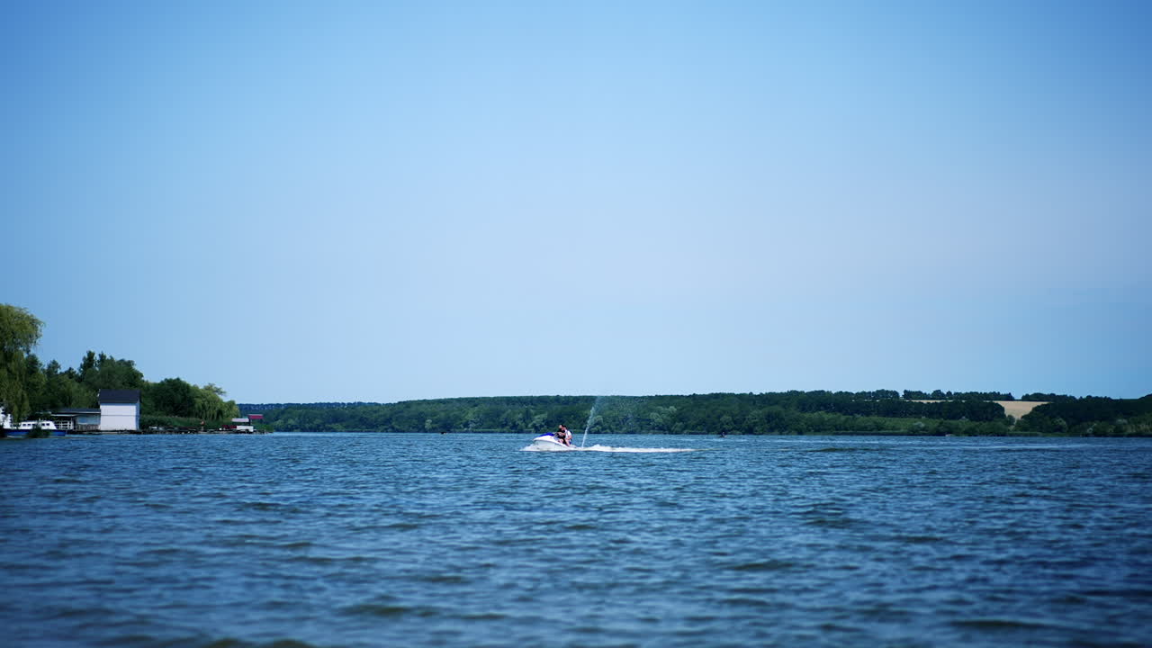 People riding jet ski water bike on the river on sunny day. Two water bikers slowly approaching the waterfront.