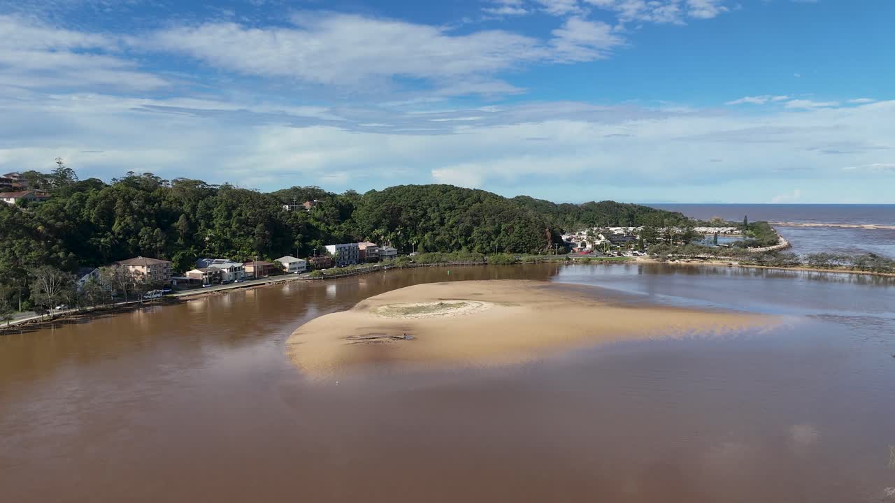 Vídeo aéreo de drone deslizando sobre o estuário do Rio Nambucca, banco de areia, vegetação e casas costeiras.