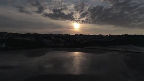 Evening-cloudy-golden-sunset-colours-across-Benllech-beach-silhouette-coastline-Anglesey-aerial-slow-lowering-view