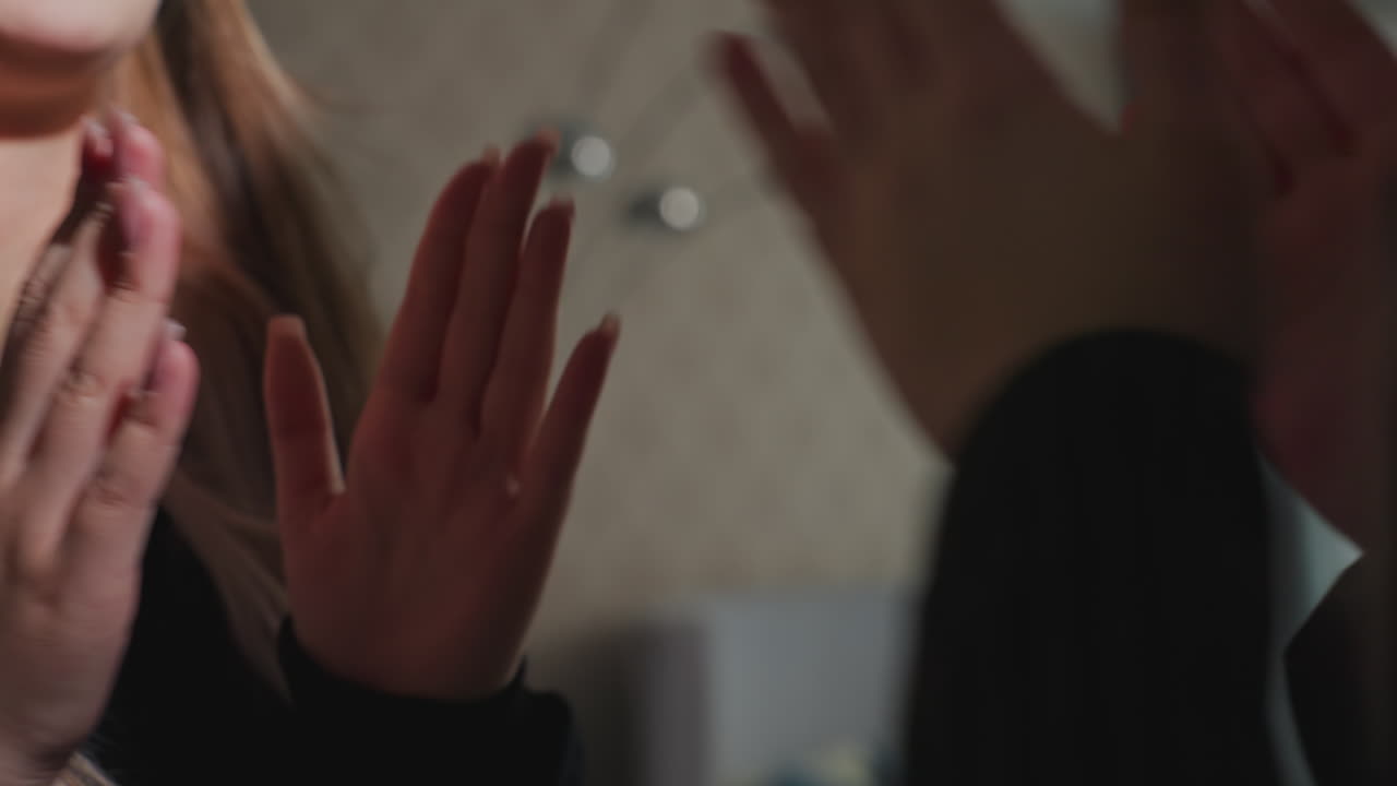 close up of student smiling as she gives high five to partner in cozy indoor setting with wallpaper and ambient lighting, focus on hands and facial expression conveying joyful interaction