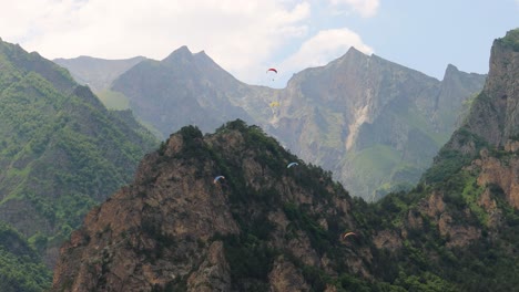 paragliding pilots fly paragliders among clouds and green mountains.