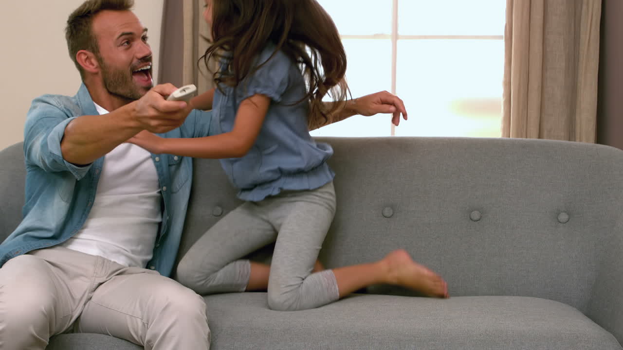 Glad far og datter bruger fjernbetjening i sofaen