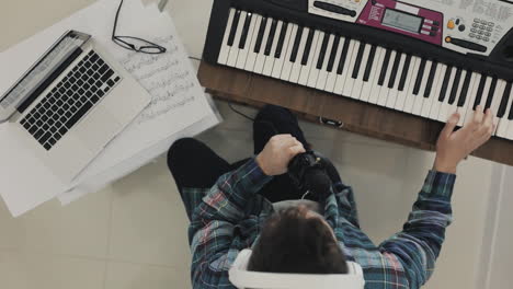 young male musician creating music, singing and playing electric keyboard at home