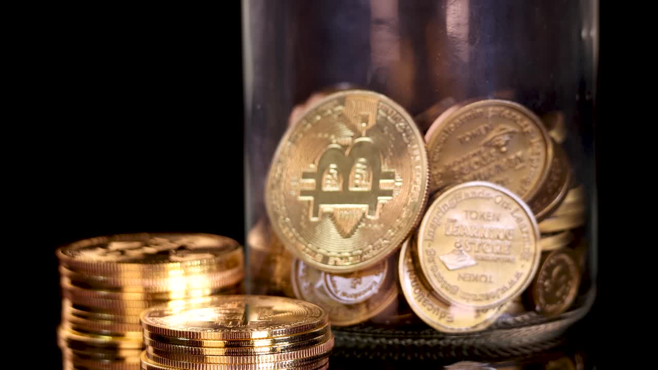 Golden and silver cryptocurrency tokens fill a glass jar under warm studio lighting, static shot