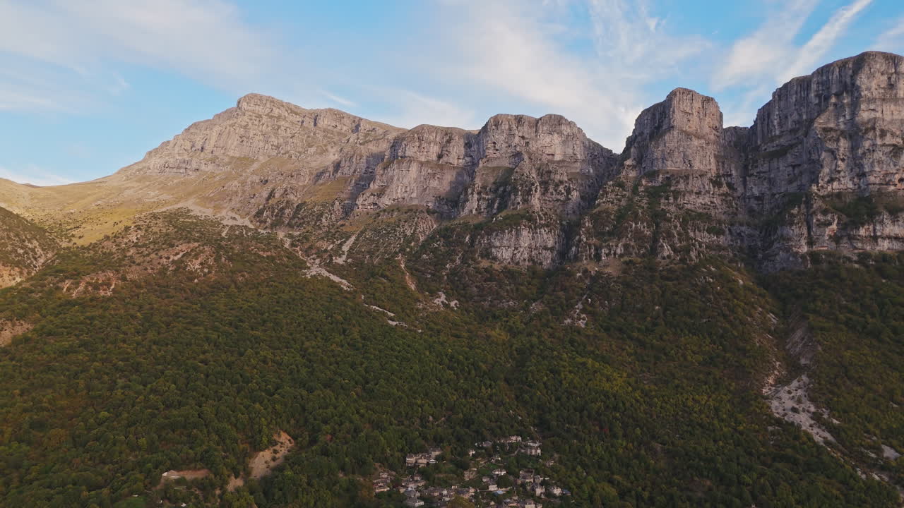 Aerial overview of Zagori mountains near Papigo, showcasing rugged peaks under a clear blue sky with tiny village nestled below